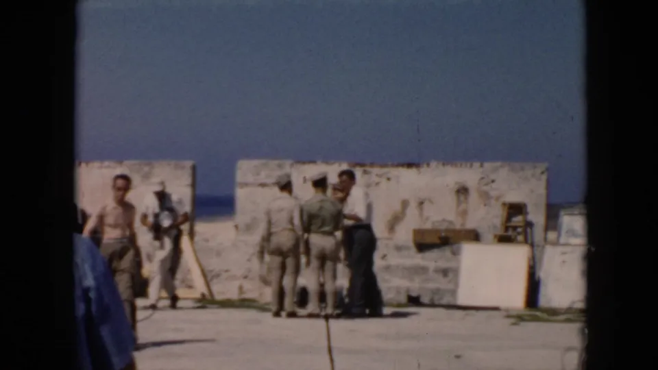 A group of men in light shirts and hats stand in a sunlit Cuba fortress area in 1956 8mm footage.