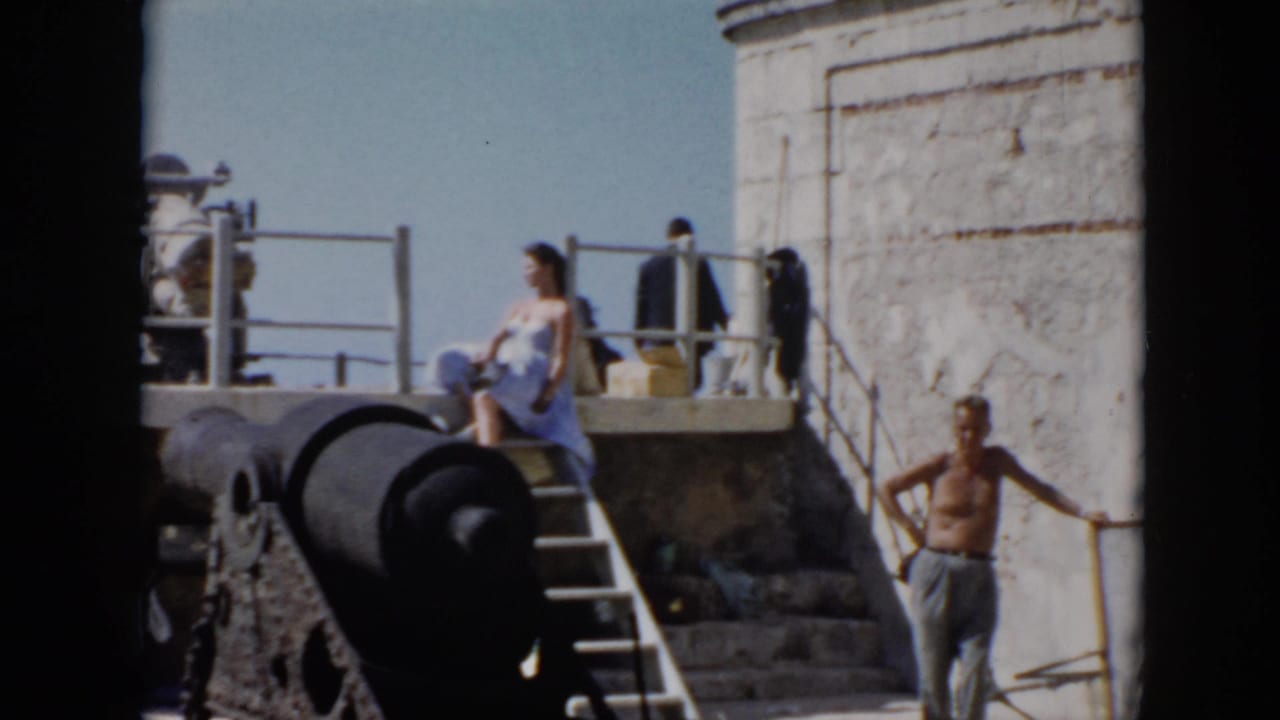 1956 Cuba home-movie frame showing a sunny stone fort courtyard with cannon, stairs, railings, and visitors near the wall.