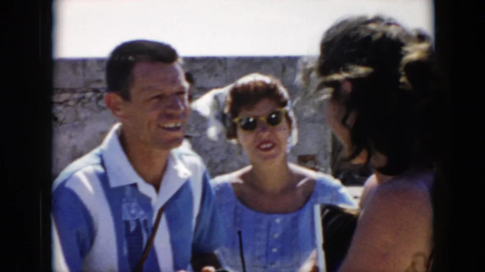 A smiling man and a woman in sunglasses talk with another woman in 1956 Cuba home-movie footage under bright daylight.
