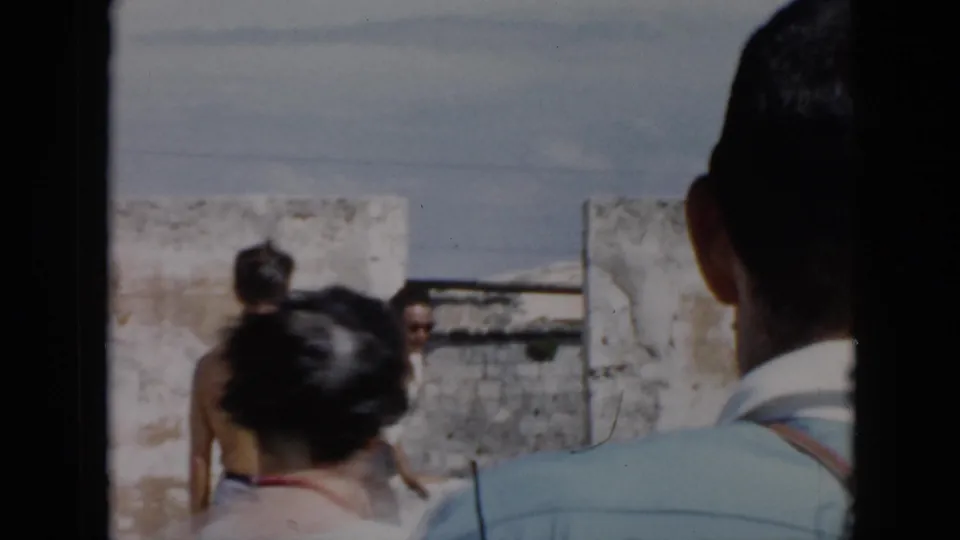 Adults move through or observe a sunlit stone-walled outdoor space in 1956 Cuba home-movie footage.