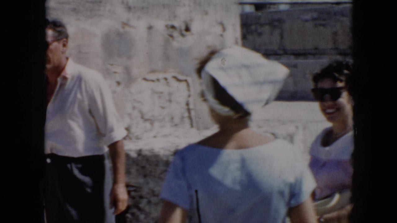 1956 Cuba home-movie frame showing adults near weathered stone ruins, including a woman in a striped headscarf and a man partly at left.