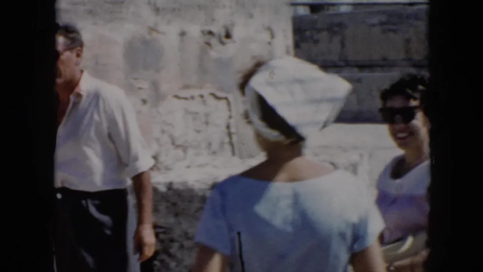 1956 Cuba home-movie frame showing adults near weathered stone ruins, including a woman in a striped headscarf and a man partly at left.