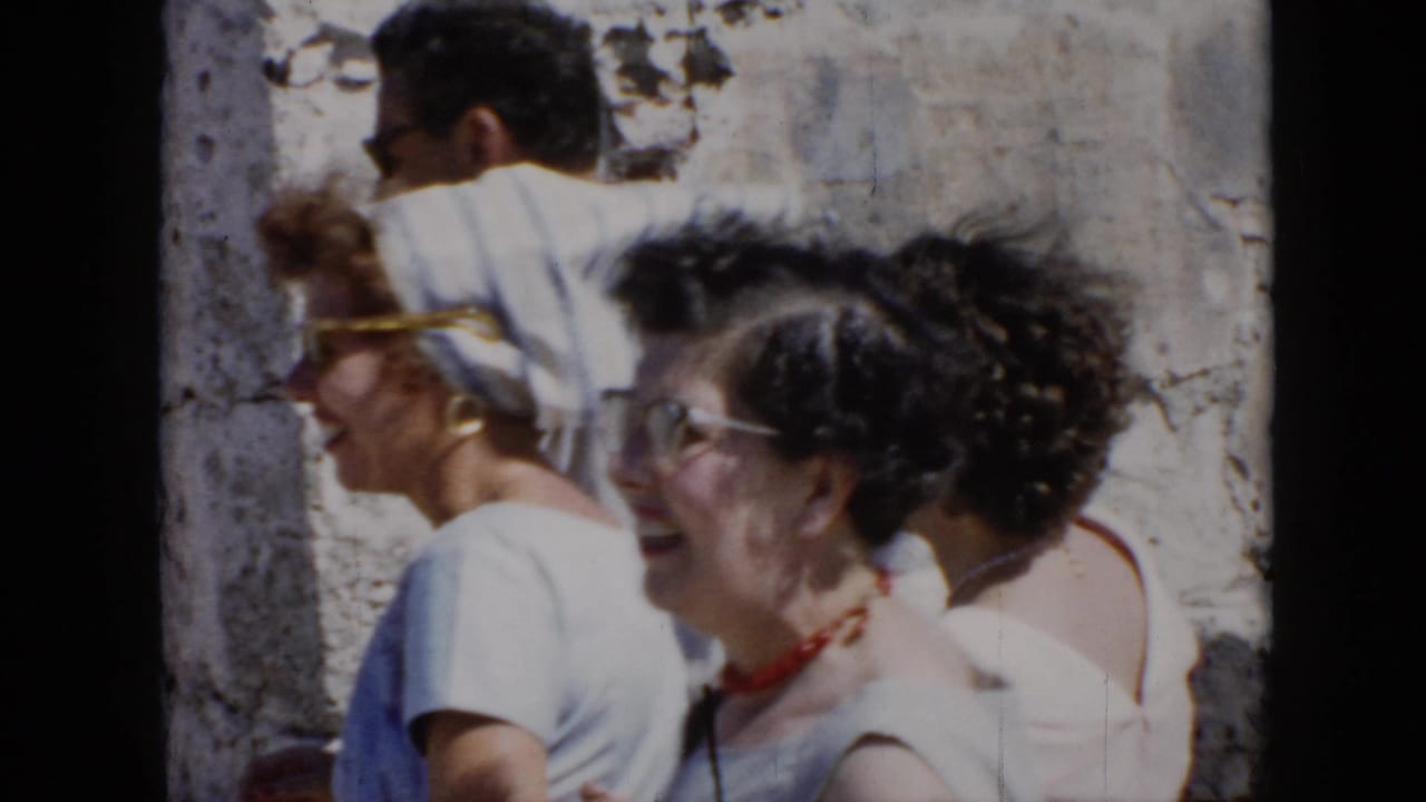Women and a man pass in front of a rough stone wall.