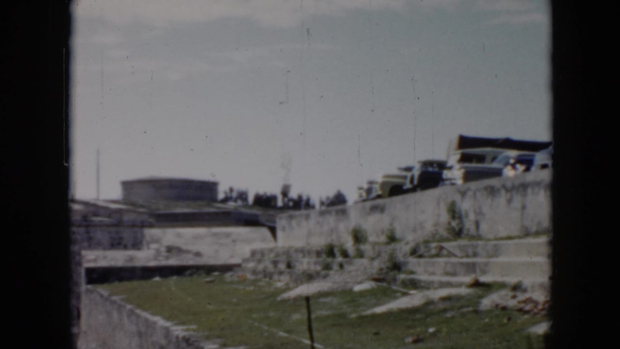 Parked cars above a stone wall with grass and a distant low building.