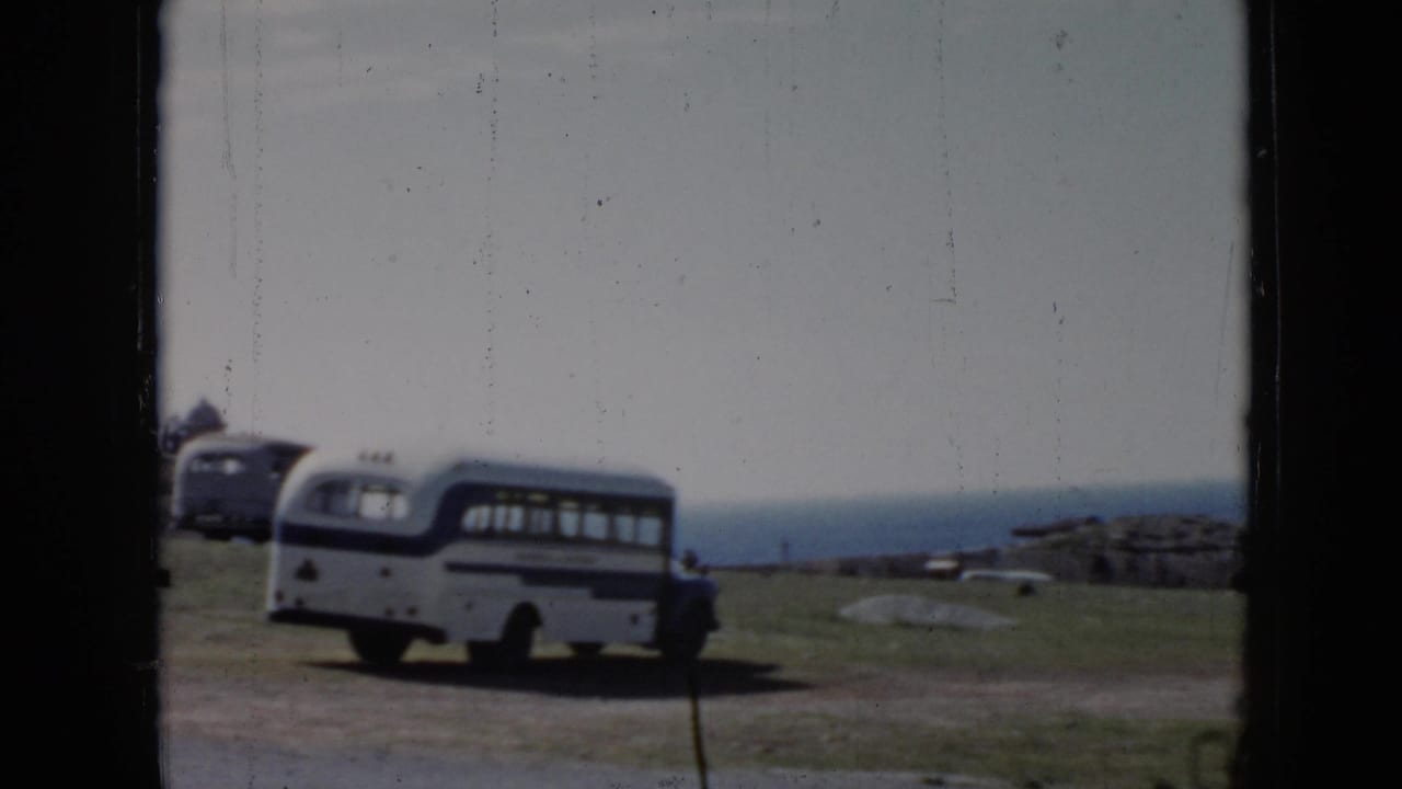 1956 Cuba home-movie frame showing a white and blue bus near a grassy cliffside overlook, filmed through dark frame edges.