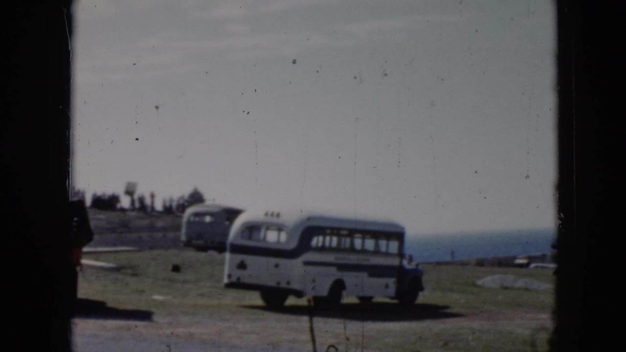 1956 Cuba frame with a parked bus on grass above the ocean, partially divided by a dark window or film-frame edge.