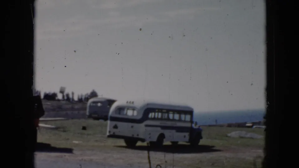 1956 Cuba frame with a parked bus on grass above the ocean, partially divided by a dark window or film-frame edge.