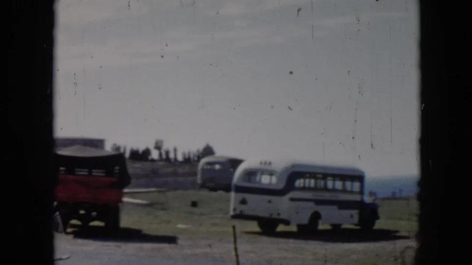 1956 Cuba home-movie frame showing a red vehicle and a white and blue bus on a rural coastal overlook.