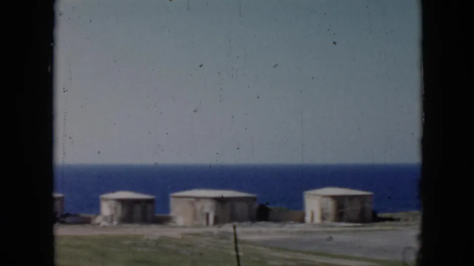 1956 Cuba frame looking past low concrete structures toward the ocean from a roadside coastal area.