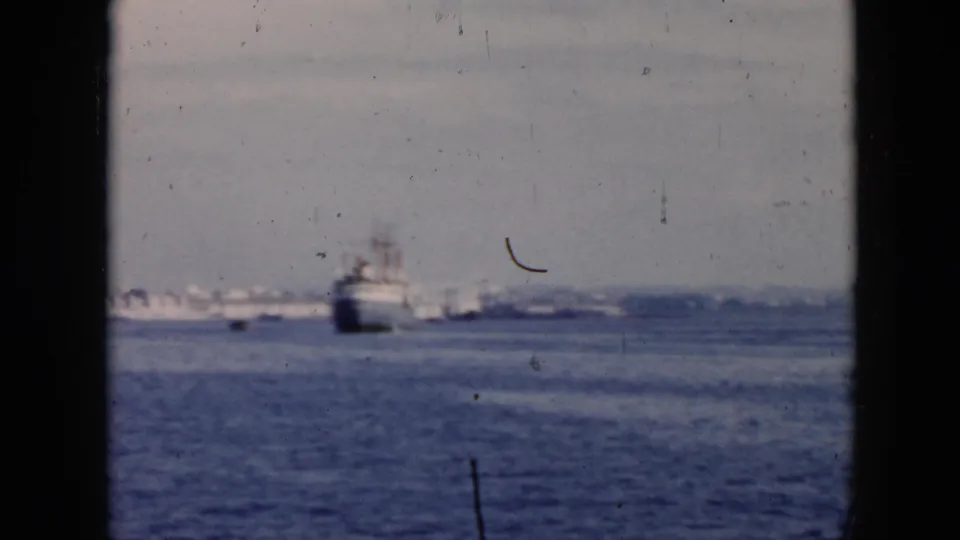 1956 Cuba 8mm frame showing a large ship offshore, seen across blue water with a faint distant shoreline and visible film wear.