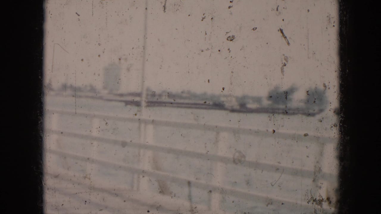 White boardwalk railing faces a hazy waterway and distant shore.