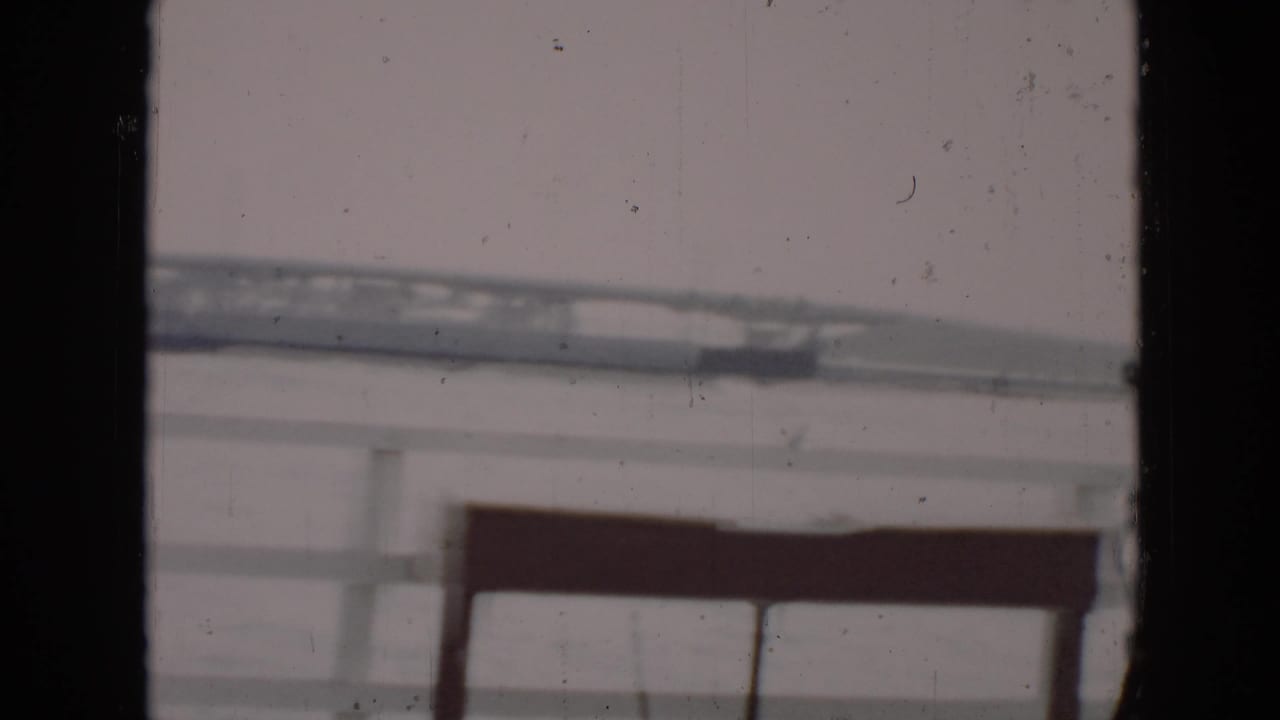 1956 Cuba home-movie view of a distant bridge over calm water, partly obscured by dark frame edges and aged film texture.
