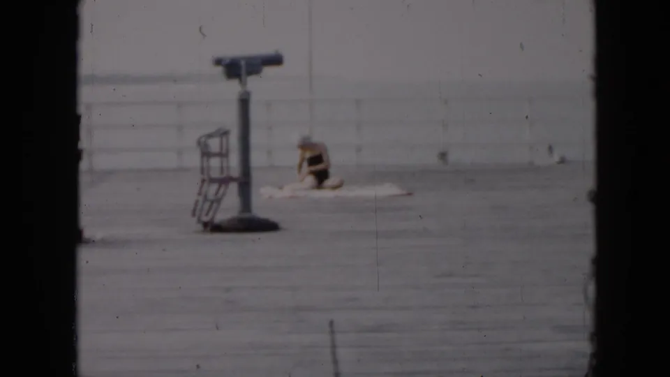 1956 Cuba pier frame showing a telescope viewer on the deck and a seated person near the white railing by the ocean.