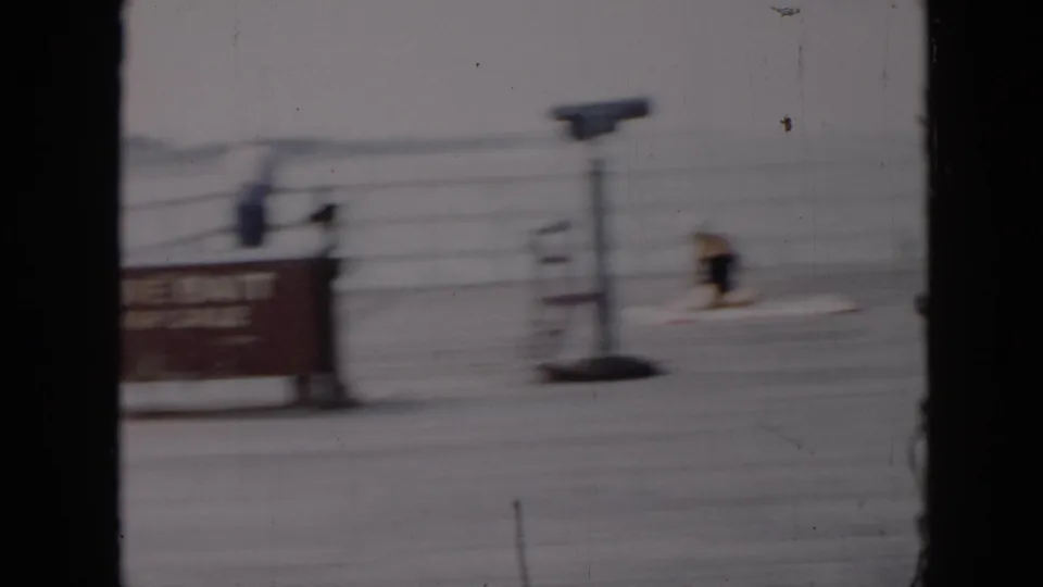 1956 Cuba home-movie frame showing a blurred dockside waterfront view beside a boat, with the woman at the helm partly visible on the right.