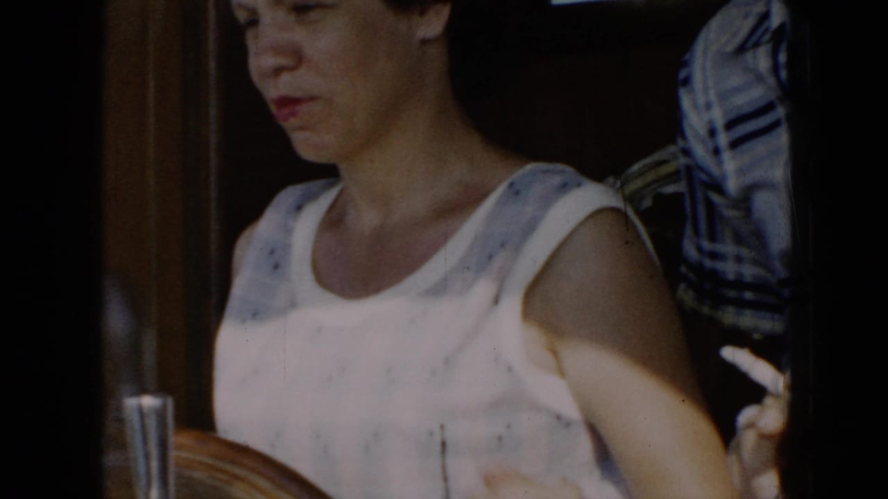 Woman in a sleeveless white patterned top stands at a wooden boat helm.