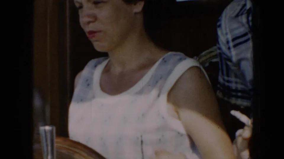 1956 Cuba frame of a woman in a sleeveless white top with blue pattern standing at a wooden boat helm, looking focused.