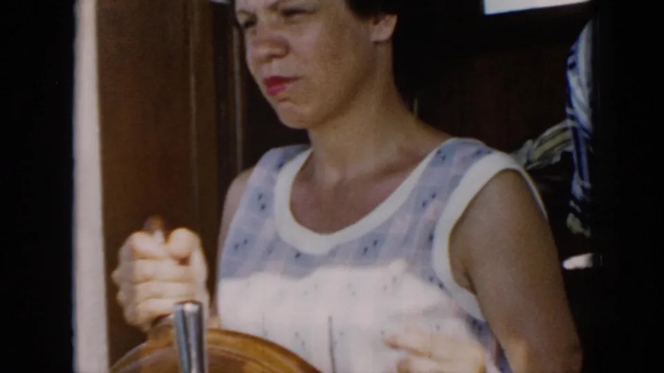 1956 Cuba frame showing the woman holding the boat's wooden wheel, with interior wood trim and fabric visible behind her.
