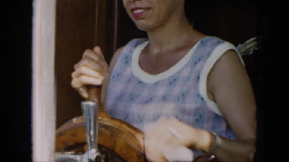 The 1956 Cuba home movie shows a close view of the woman gripping the wooden ship's wheel, with soft 8mm focus and boat trim around her.