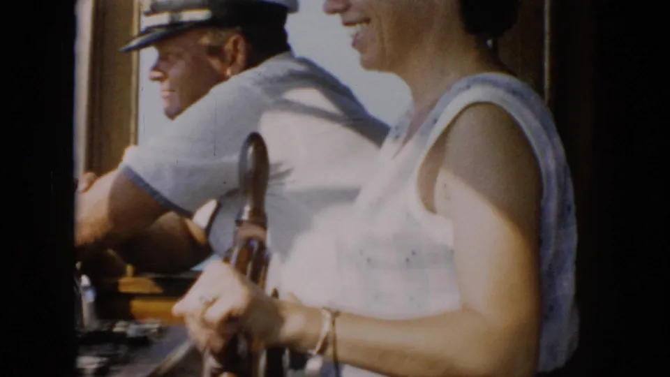The final frame shows the woman smiling at the wheel while a man in a light shirt and cap stands beside her in bright daylight on the boat.