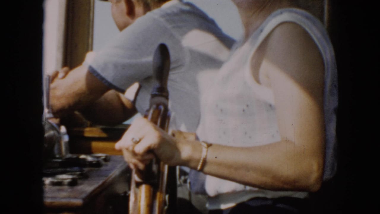 1956 Cuba 8mm frame showing a woman at a wooden ship wheel beside a man inside a sunlit bridge.
