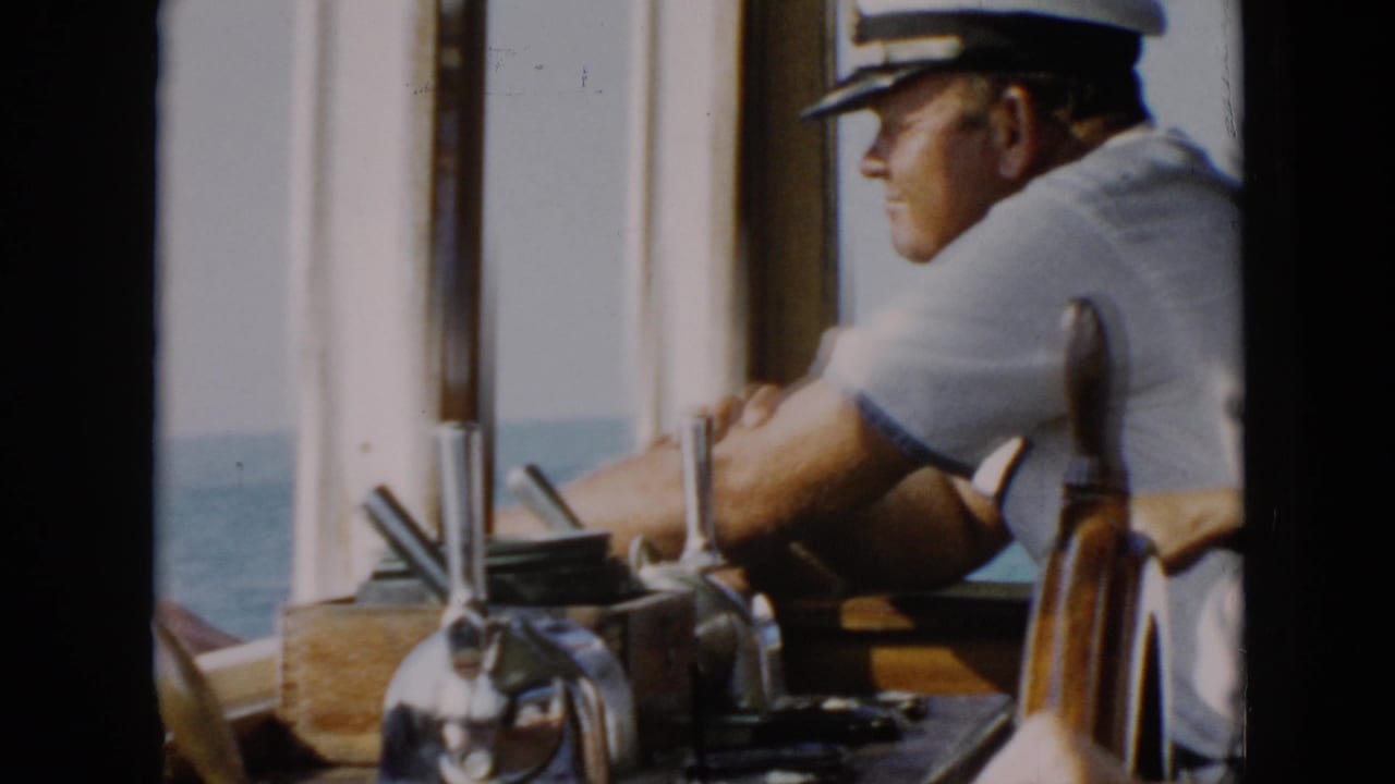 1956 Cuba ship bridge view with a uniformed crewman in a white cap near chrome controls and open water.