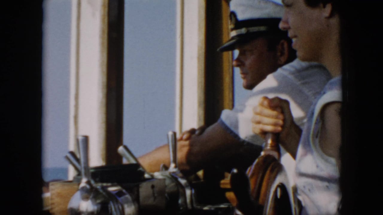 1956 Cuba-associated 8mm frame showing a sailor in a white cap steering inside a wheelhouse with water beyond the windows.