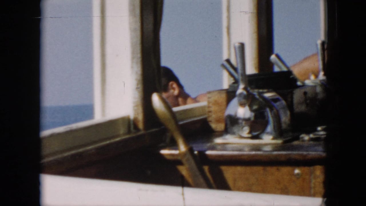 1956 Cuba-associated home-movie frame looking across the wheelhouse, with steering gear, windows, and a partial view of crew by the sea.