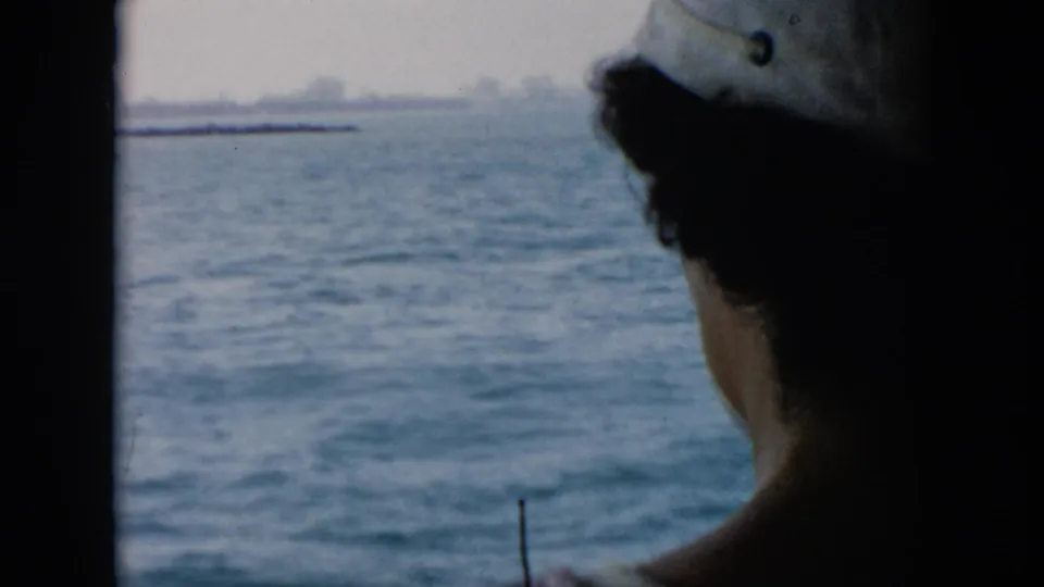 1956 Cuba-associated home-movie frame with a partial foreground figure and a calm ocean view through the vessel window.