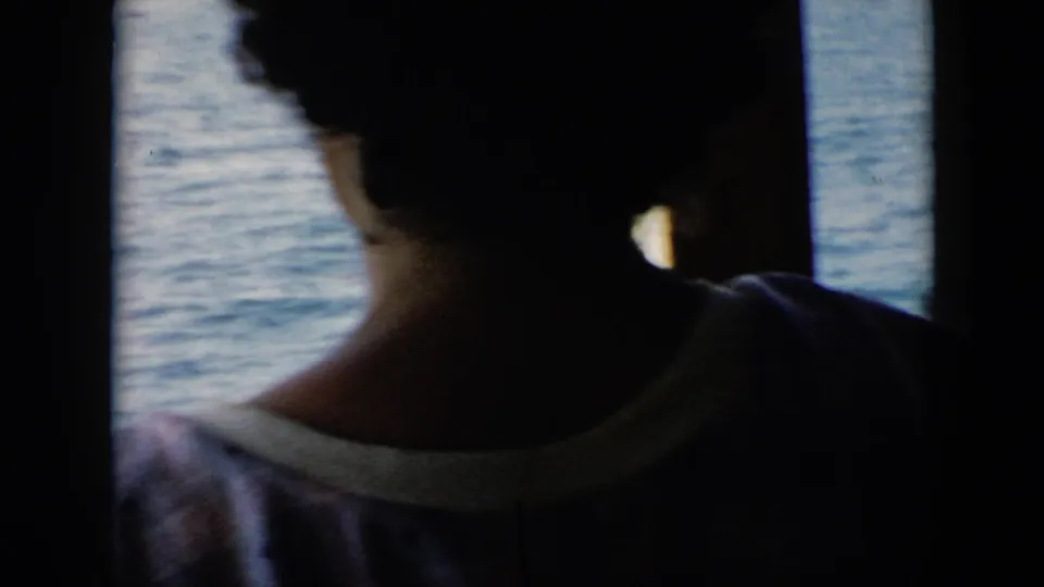 A silhouetted passenger aboard a boat in Cuba, 1956, faces the water through a dark window frame.