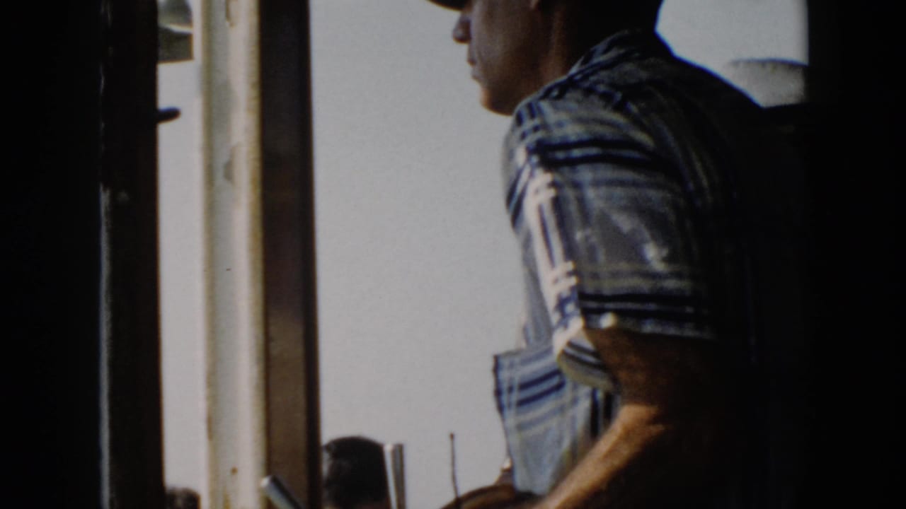 Man in a striped shirt stands at the helm with his arm near the wheel.