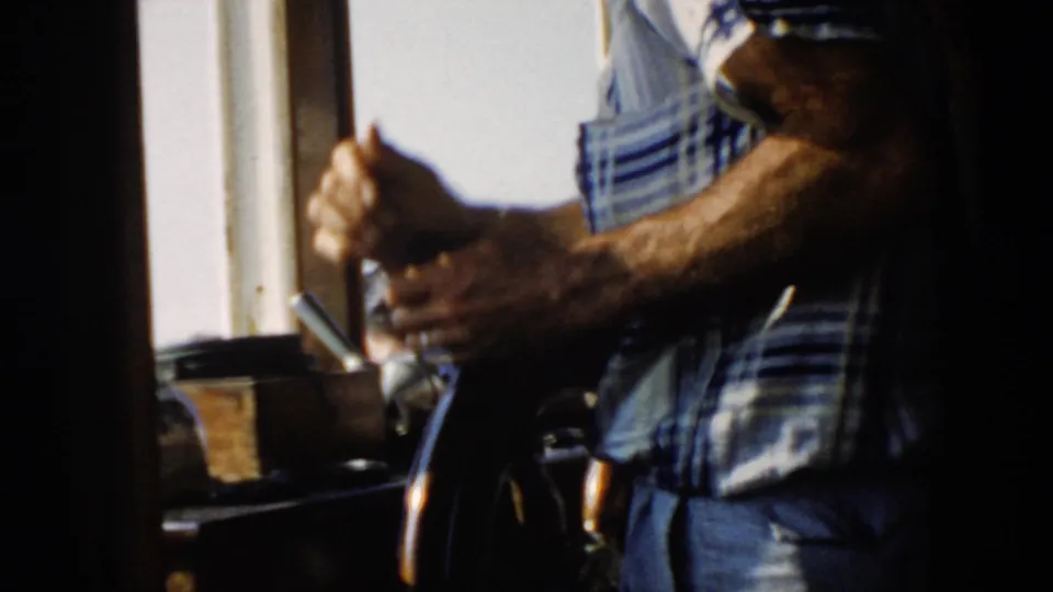 A close 8mm frame shows the man's arm gripping the wheel while he steers the boat from inside the bright wheelhouse.