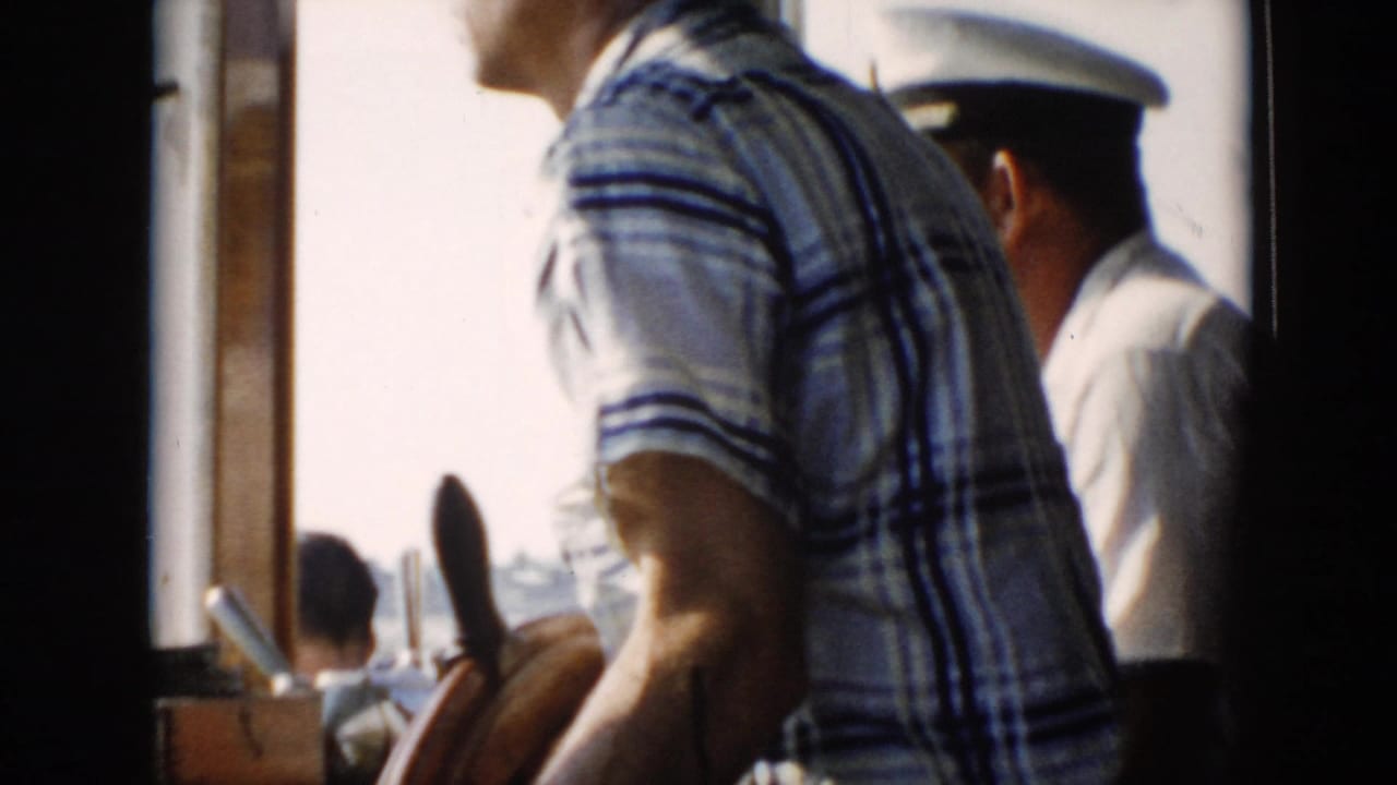 1956 Cuba 8mm frame showing a close passenger view on a boat, with a plaid-shirted figure and a white-capped person near the cabin edge.