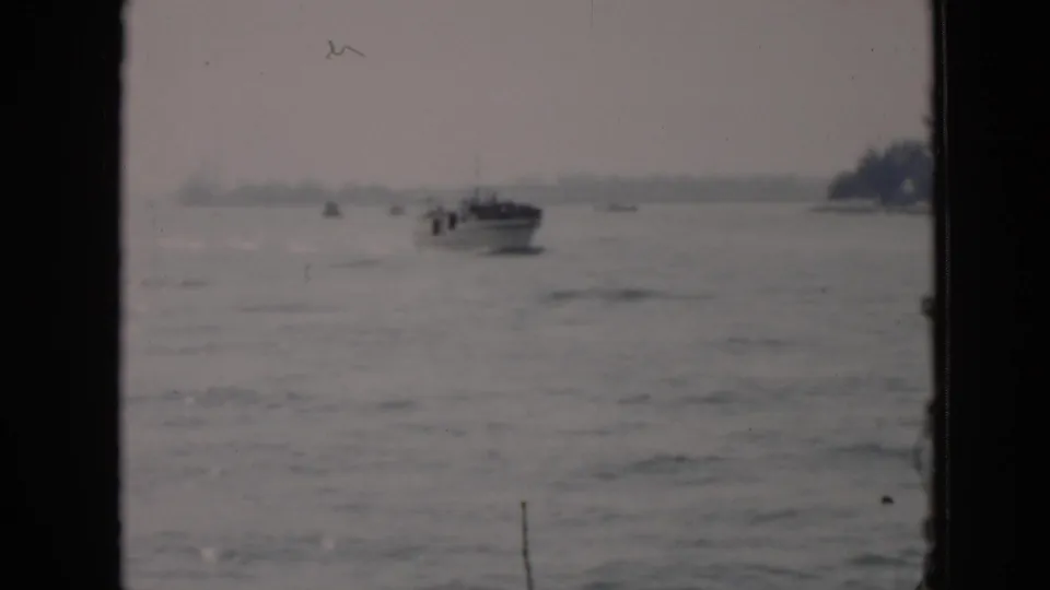 1956 Cuba 8mm frame showing a small motorboat in the distance on calm river or lake water with a hazy shoreline beyond.