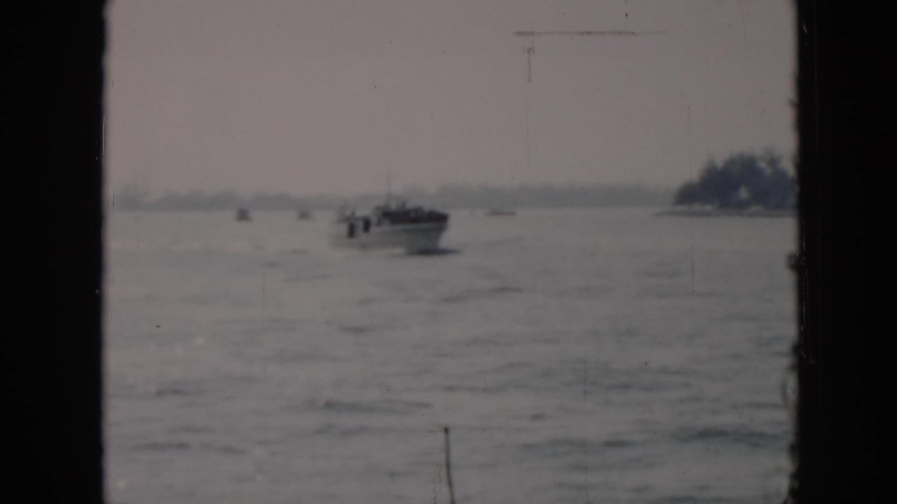 A distant motorboat crosses choppy water in Cuba, 1956, with a tree-lined shore faintly visible beyond the window-framed view.