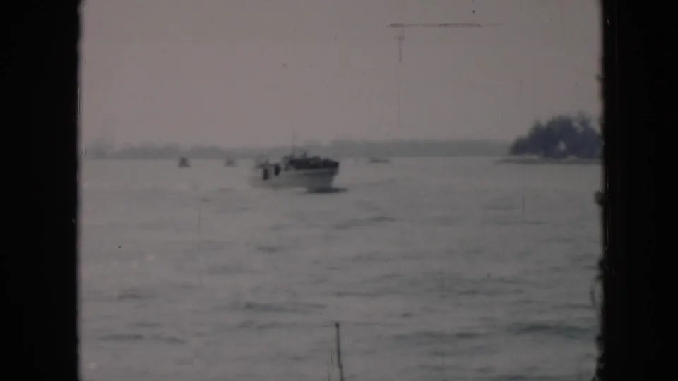 A distant motorboat crosses choppy water in Cuba, 1956, with a tree-lined shore faintly visible beyond the window-framed view.