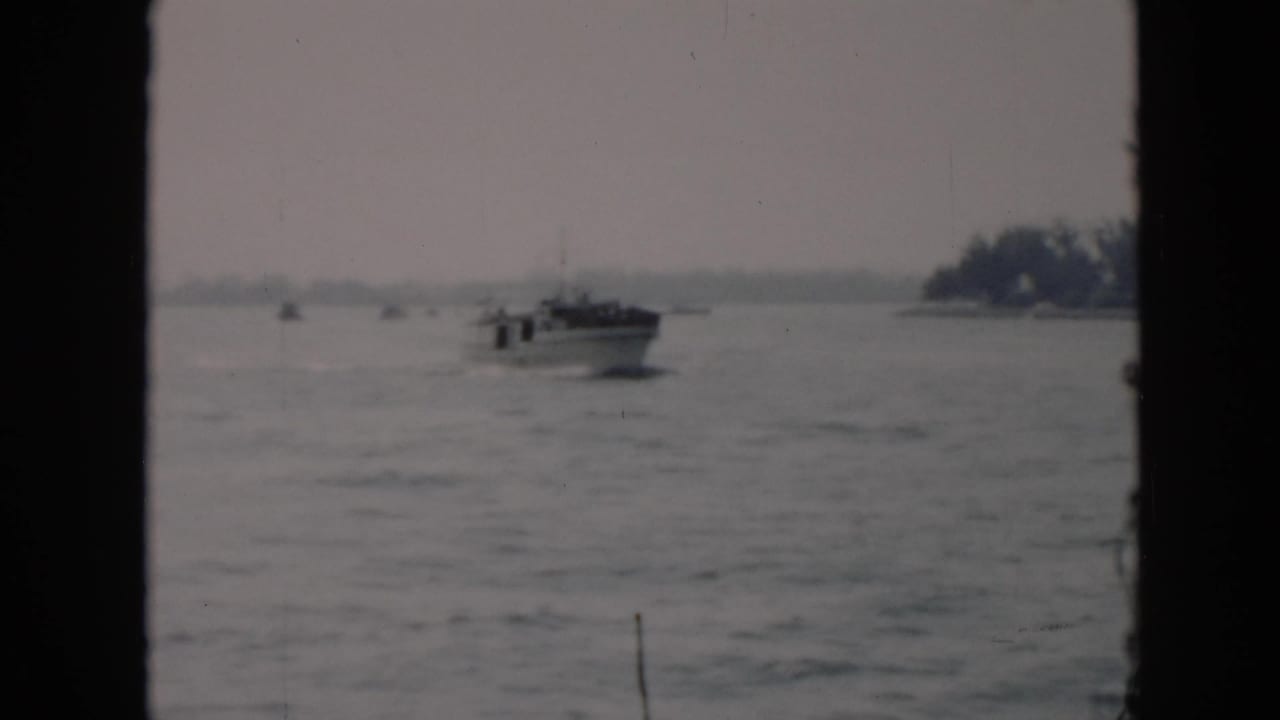 The motorboat continues across choppy Cuban coastal water, framed by dark vertical film or window borders with trees on the horizon.