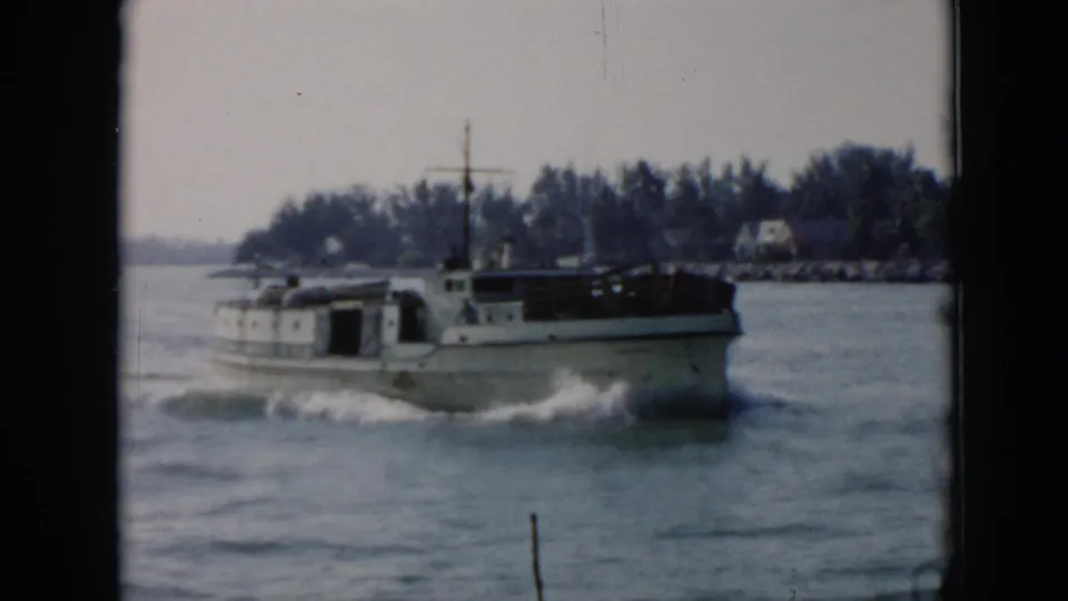 The white cabin motorboat moves past a wooded Cuban shoreline, its bow cutting through choppy water in soft 8mm color.