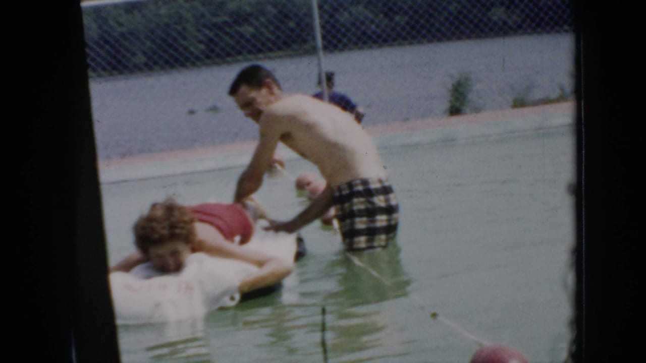 In 1956 Cuba home-movie footage, one young man leans over another on a white pool raft while a chain-link fence stands behind them.