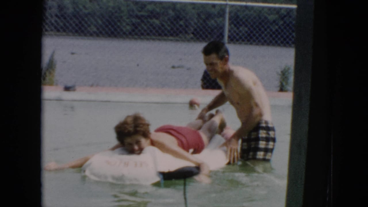 1956 Cuba 8mm frame showing a man pushing a woman in a red swimsuit on a white float in a shallow outdoor pool.
