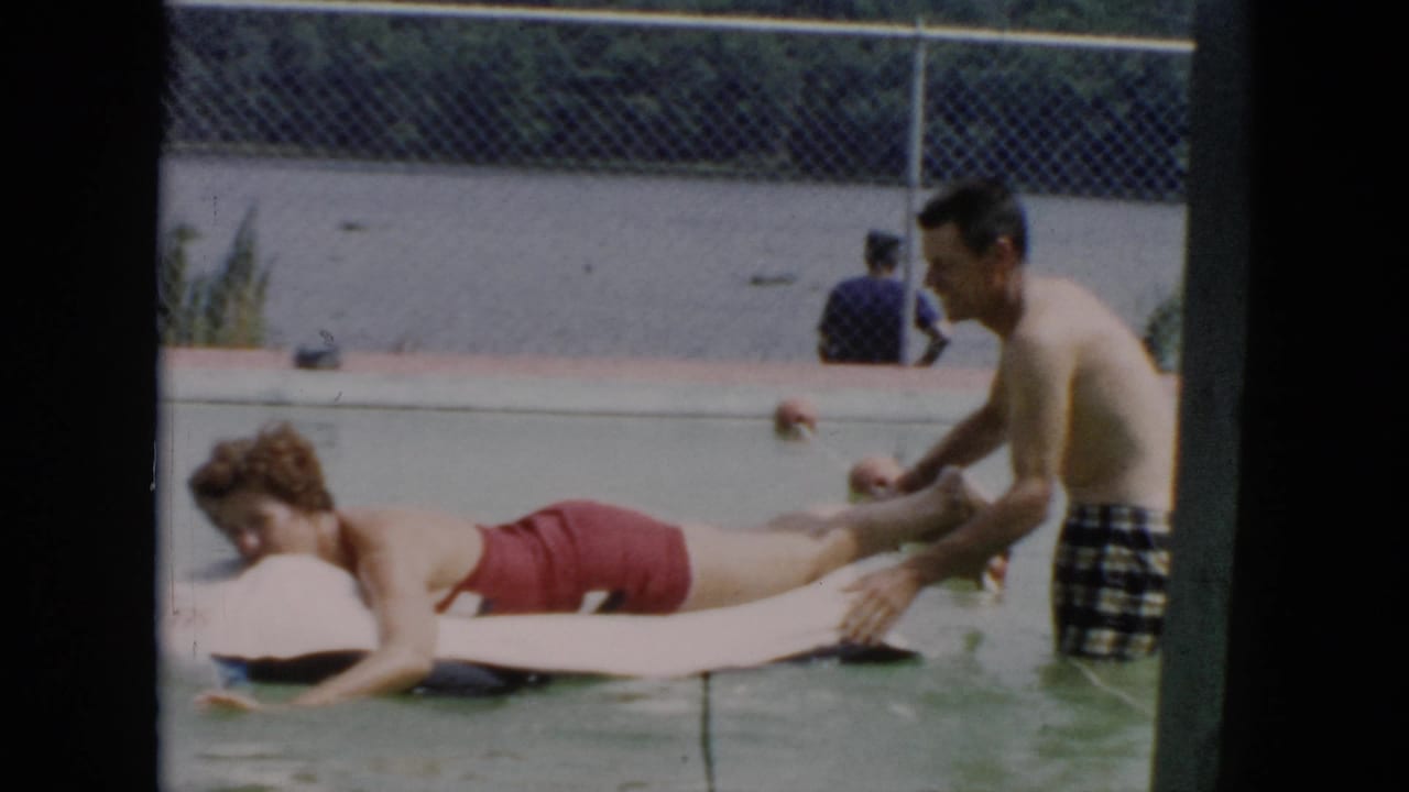 Woman lies on a white float while a man holds her feet in the pool.