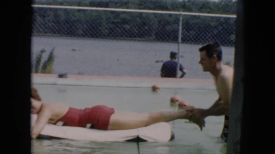 1956 Cuba 8mm frame showing the woman partly cropped on a white float while the man pushes from the side of the pool.