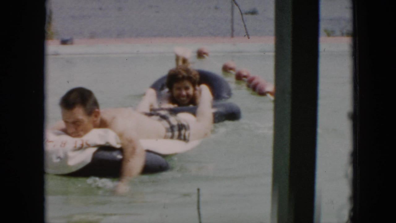 1956 Cuba frame of adults floating on black inner tubes in calm water, seen through a window or structural frame.