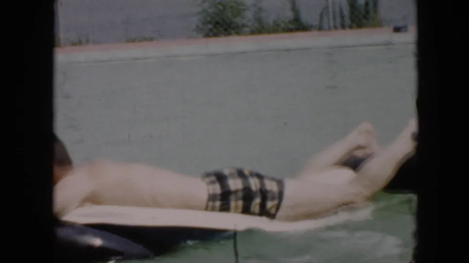 1956 Cuba home-movie frame showing a man stretched across an inflatable tube, partly cropped by dark foreground framing.