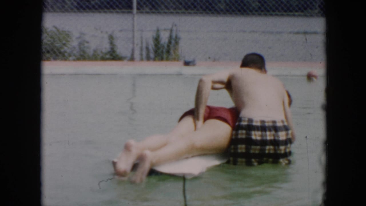 1956 Cuba 8mm frame showing two people in a swimming pool, with one on a white float and another seated nearby in plaid trunks.