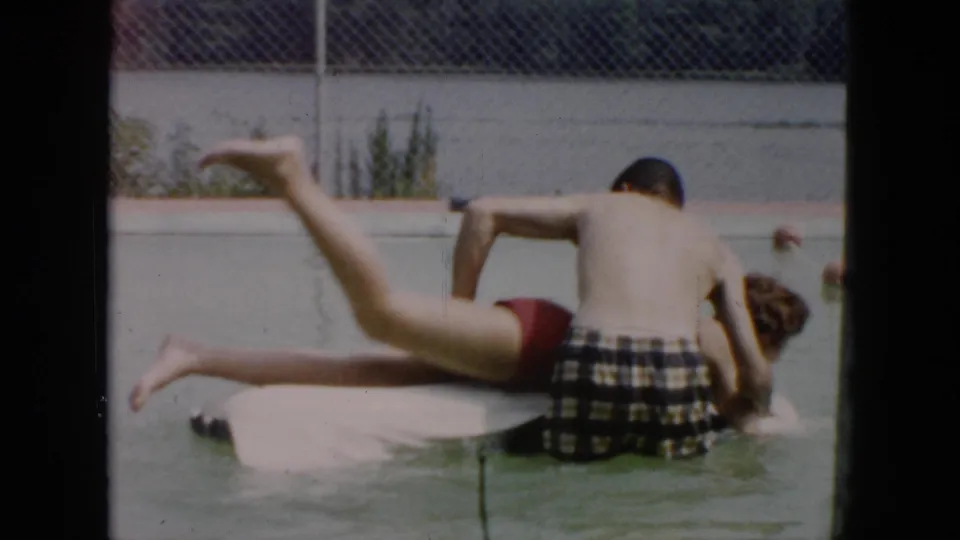 1956 Cuba home-movie frame of swimming practice in a pool, with one person kicking from a float as another supports them.