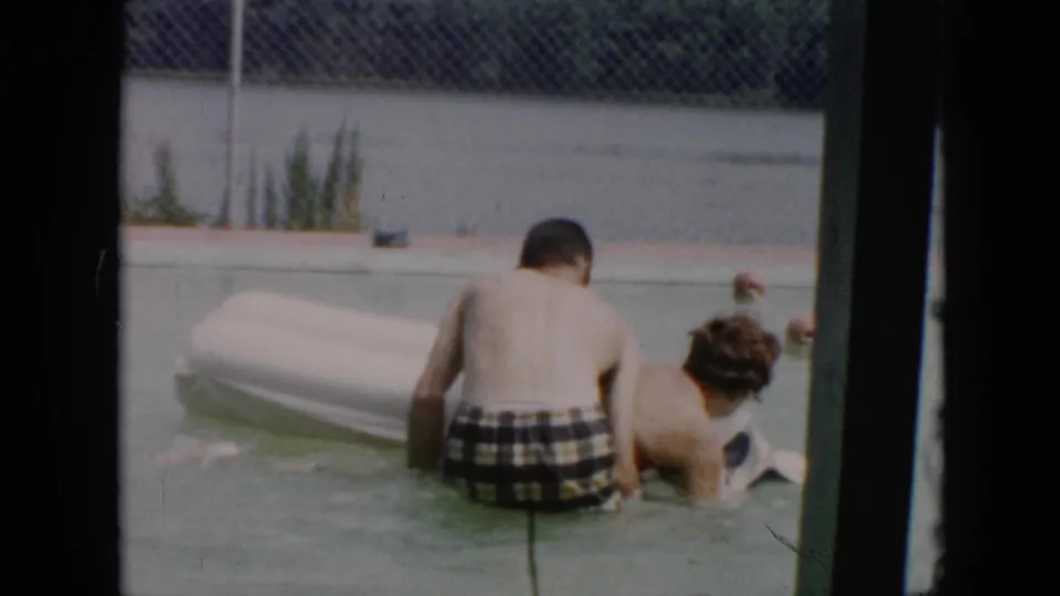 1956 Cuba 8mm frame with two swimmers close to a white float in shallow pool water, filmed from a candid home-movie angle.