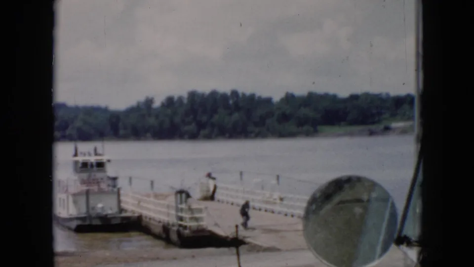 1956 Cuba home-movie frame showing a dock and small boat on the water, with trees in the distance and a round foreground object.