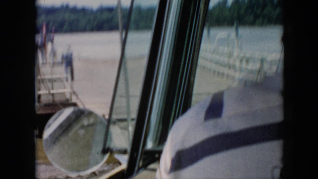 Window-framed view of a dock and river with a light-shirted person at the edge of the frame.