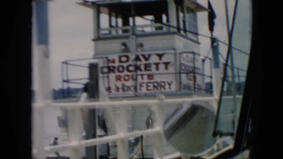 1956 Cuba home-movie frame with a visible Davy Crockett Route Ferry sign on the ferry pilothouse, framed by railings and vehicle glass.