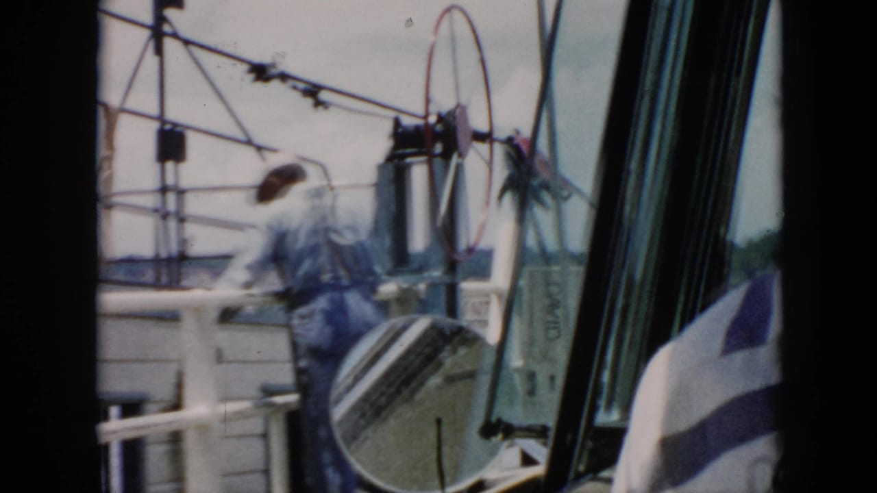 1956 Cuba home-movie frame from inside a car, looking through the windshield at a ferry crew member, deck railings, and equipment.